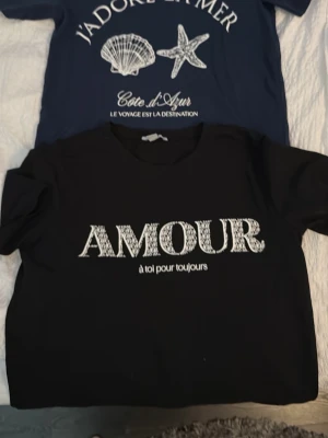 Blå och Svart t-shirt med texten AMOUR - Svart t-shirt med vit texten 'AMOUR à toi pour toujours' framtill. Klassisk rund halsringning och korta ärmar. Perfekt för en avslappnad och trendig look. 2 st en svart och en blå enligt bild. 