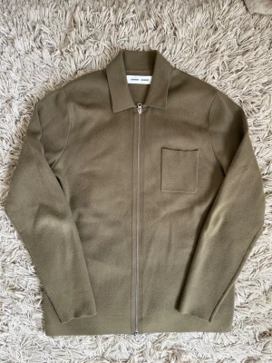 Olivgrön overshirt från Samsoe - Stilren olivgrön overshirt från Samsoe Samsoe med rak passform, dragkedja framtill och en bröstficka. Tillverkad i ett mjukt, strukturerat material som ger en avslappnad men snygg look. Perfekt att bära över en t-shirt eller skjorta.