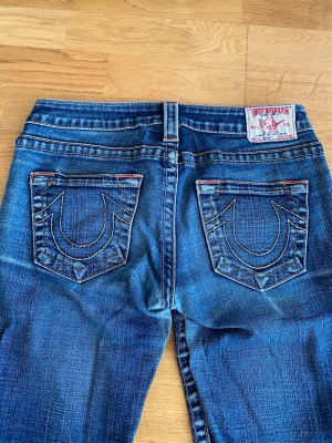Blå True Religion jeans med kontrastsömmar - Säljer ett par blå jeans från True Religion med ikoniska kontrastsömmar på bakfickorna och klassisk femficksdesign. Jeansen har låg midja och raka ben. Nypris runt 1300kr. Jag är runt 160 och de passar bra🌸