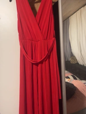 Plisserad jumpsuit omlott röd & svart - Säljer två snygga plisserade jumpsuits med omlott-ringning och breda ben. Finns i både rött och svart, med ett matchande bälte i midjan. Materialet är mjukt och faller snyggt, perfekt för dig som vill ha en cool och trendig look. Använt bara en gång båda köpte för 1000kr styck. Storlek S passar också som M säljer båda för 800kr
