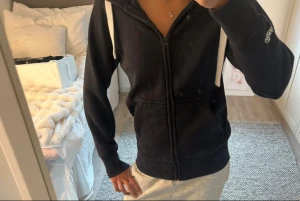 Svart hoodie med dragkedja och huva - Svart hoodie från russemerch i storlek S. Modellen har dragkedja framtill, två stora fickor och vita dragsnören i huvan. Tillverkad i mjukt material som känns skönt mot huden. Perfekt för en avslappnad och chill stil.