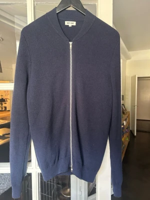 Mörkblå ziptröja från Soft Goat - Mörkblå ziptröja från Soft Goat i mjuk och lyxig ullmix. Tröjan har hel dragkedja framtill, ribbade muddar och en stilren, minimalistisk design. Perfekt för lager-på-lager och enkel att matcha med olika outfits.