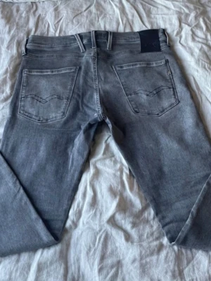 Grå jeans från Replay, modell Anbass - Snygga grå jeans från Replay, modell Anbass. Jeansen har klassisk femficksdesign, raka ben och diskreta slitningar. Tillverkade i mjuk denim med Replay-logga på fickan och bak vid linningen. Perfekta för en avslappnad och trendig look.