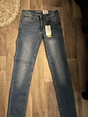 Blå slim fit jeans från Garcia - Snygga blå slim fit jeans från Garcia med klassisk femficksdesign och ljus tvätt. Jeansen har normal midja, raka ben och detaljerade sömmar på bakfickorna. Tillverkade i mjuk och stretchig denim för skön passform. Perfekta för en avslappnad och trendig look. Aldrig använda enbart testade