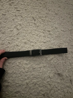 Svart klassiskt bälte i skinn - Snyggt svart bälte i skinn med enkel, fyrkantig metallspänne. Bältet har en stilren och tidlös design som passar till de flesta outfits. Insidan är brun vilket ger en snygg kontrast. Perfekt accessoar för att lyfta din look.