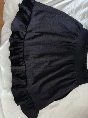 Svart volangkjol med struktur - Kort svart kjol med volangkant och strukturerat tyg. Kjolen har bred resår i midjan för skön passform och en lätt glansig yta. Perfekt för dig som gillar trendiga och feminina plagg. Tveka inte på att höra av dig om du har några frågor!💕 svarar snabbt!