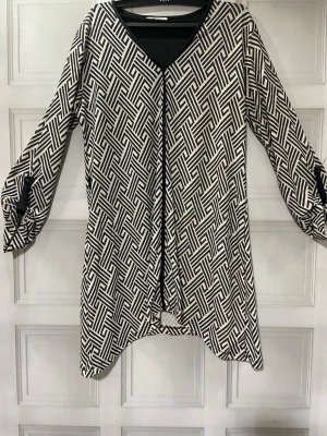 Svartvit mönstrad blus med V-ringning - Snygg svartvit blus med grafiskt mönster och V-ringning. Blusen har långa ärmar med dekorativa knytband vid ärmsluten och svarta detaljer längs kanterna. Materialet känns mjukt och följsamt, perfekt för en trendig och avslappnad look.