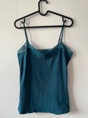 Turkos linnetopp med spetskant - Turkos linnetopp med tunna axelband och dekorativ spetskant upptill.