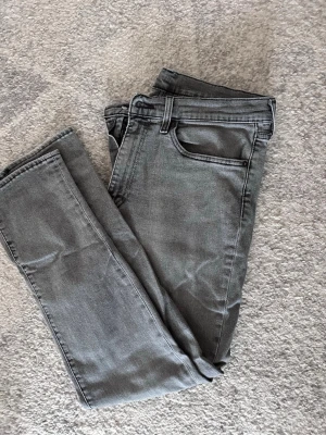 Grå jeans från Levi's - Säljer ett par snygga grå jeans från Levi's med klassisk femficksmodell och raka ben. Jeansen har en cool tvättad look, Levi's-lapp bak i midjan och den ikoniska röda etiketten på bakfickan. Perfekta till en avslappnad stil. W 34 L 30 
