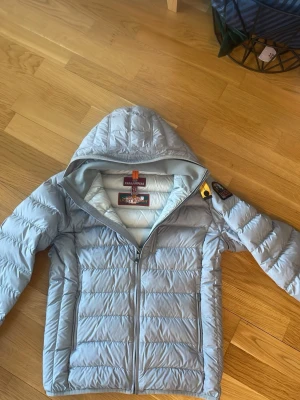Ljusgrå  dunjacka från Parajumpers - Snygg ljusgrå dunjacka från Parajumpers med quiltad design och dragkedja framtill. Jackan är superlätt och har en klassisk patch på ärmen samt två sidofickor. Perfekt för kalla vinterdagar och riktigt stilren.