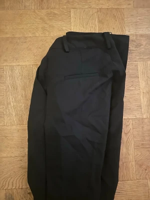 Svarta kostymbyxor från BikBok - Snygga svarta kostymbyxor från BikBok med klassisk rak passform och diskreta fickor bak. Byxorna har hällor för skärp och stängs med dragkedja och knapp. Perfekta för en clean och stilren look.