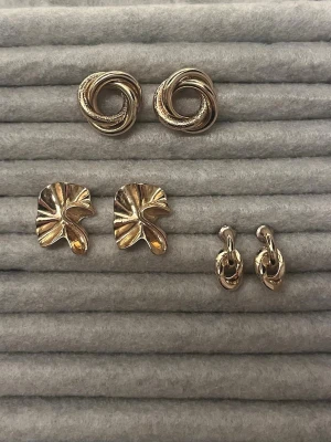 Guldiga örhängen  - Säljer ett par snygga örhängen i guldfärgad metall med tvinnad, cirkelformad design. Perfekta för att ge din look en elegant touch. Passar dig som gillar stilrena accessoarer med en twist.