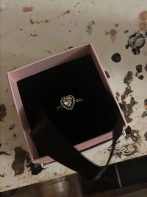 Silverring med hjärta från Pandora - Snygg silverring från Pandora med ett glittrande hjärta i mitten, omgiven av små gnistrande stenar. Ni får även med en påse från Pandora. Priset kan sänkas. 