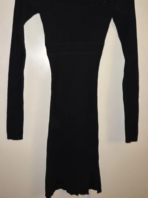 Svart ribbad långärmad klänning - Tajt svart ribbad klänning med lång ärm och rund halsringning. Klänningen är figurnära och har en enkel, stilren design som passar perfekt till olika tillfällen. Materialet är stretchigt och bekvämt.