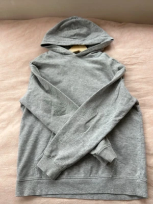Grå basic hoodie med huva - En enkel och stilren grå hoodie med huva och långa ärmar. Ribbstickade muddar vid ärmslut och nederkant. 
