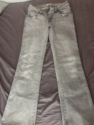 Lågmidjade grå jeans från lager med mönster  - Säljer ett par grå lågmidjade flare jeans med snyggt slitna detaljer och broderade mönster på bakfickorna. Jeansen har klassisk femficksdesign och är tillverkade i denim med lätt stretch. Perfekta för dig som gillar en avslappnad men trendig look.