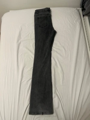 Svarta bootcut jeans med slitning - Säljer ett par svarta bootcut jeans med lätt tvättad look och en liten slitning på ena benet. Jeansen har klassisk femficksdesign och raka, utsvängda ben. Perfekta för dig som gillar en avslappnad men trendig stil.