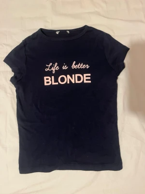 Marinblå t-shirt med texttryck - Marinblå t-shirt med rosa texten 'Life is better BLONDE' på bröstet. Klassisk rund halsringning och korta ärmar. Perfekt för dig som gillar statement-plagg och enkel stil.