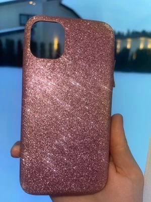 Glittrigt rosa mobilskal iPhone 11 - Säljer ett snyggt mobilskal i glittrigt rosa med slät insida. Skalets yta är täckt av glitter som ger en riktigt festlig look. Passar perfekt för dig som vill ha ett skal som sticker ut och skyddar mobilen. Materialet är troligtvis plast eller silikon.