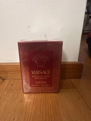 Ny Versace Eros Flame pour homme parfym 100 ml - Ny oöppnad 100 ml Versace Eros Flame pour homme är en Eau de Parfum i en lyxig röd och guld kartong med klassiskt Versace-mönster och Medusa-huvud. Flaskan innehåller 100 ml och är designad för män. Doften är intensiv och elegant, perfekt för dig som gillar exklusiva parfymer.