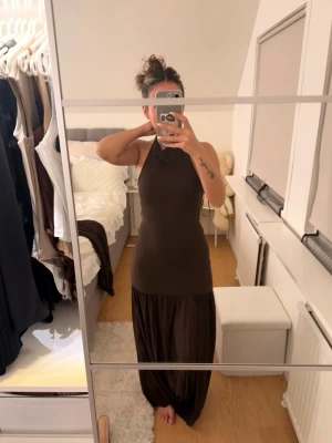 ZARA långklänning med halterneck - Snygg brun långklänning med halterneck och figurnära passform upptill. Klänningen har en lösare, flowy kjol och är ärmlös. Perfekt för dig som gillar en stilren och trendig look.
