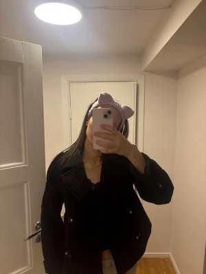 Svart dubbelknäppt kappa - Stilren svart kappa med dubbelknäppning och bred krage. Klassisk modell som passar till många olika outfits. Kappan har en rak passform och knappar framtill. Perfekt för dig som vill ha en tidlös och snygg jacka till garderoben.