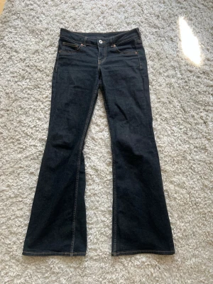 Mörkblå Lågmidjade bootcut jeans - Snygga mörkblå bootcut jeans med klassisk femficksdesign och kontrastsömmar. Jeansen har låg midja och utsvängda ben, perfekta för en trendig och avslappnad stil. Tillverkade i stretchig denim för extra komfort.