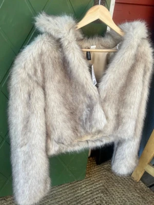 Beige kort fuskpälsjacka från H&M - Säljer en supermjuk och fluffig beige fuskpälsjacka från H&M. Jackan är kort i modellen, har långa ärmar och en bred krage som ger en lyxig känsla. Perfekt för att höja din vinterstil med en trendig look. Nypris 499