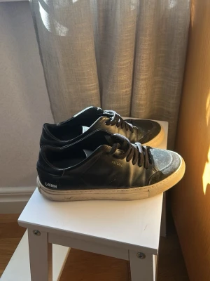 Svarta sneakers från Axel Arigato - Snygga svarta sneakers från Axel Arigato med vita sulor och diskret logga på sidan. Skorna har klassisk låg profil, svarta skosnören och är tillverkade i läder med mockadetaljer vid tån. Perfekta för en clean och stilren look.