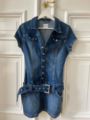 Jeansklänning med bälte från Bershka - Kort jeansklänning från Bershka med markerad midja och tillhörande bälte. Klänningen har korta ärmar, knappar framtill, två bröstfickor med lock🙌🏼använd fåtal gånger så den är som ny!💞