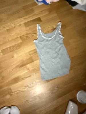 Grå ribbad linnetopp med spetskant - Snygg grå ribbad linnetopp med vit spetskant runt ringningen. Perfekt att styla till jeans eller kjol för en enkel men trendig look. Ärmlös och i mjukt material som känns skönt mot huden.