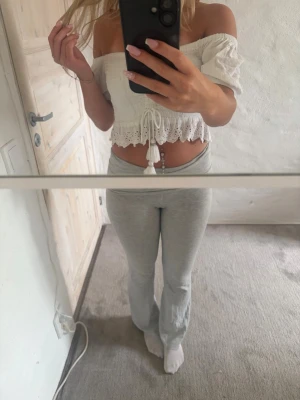 Vit offshoulder croppad blus - Säljer en söt vit offshoulder blus med croppad passform och volangkant. Toppen har snörning framtill med dekorativa tofsar och är tillverkad i ett lätt, luftigt material med spetsdetaljer. Perfekt för sommarens alla tillfällen!