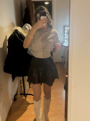 Svart volangkjol i skinnimitation - Svart minikjol i skinnimitation med markerad midja och volangdetaljer framtill. Baksidan är slät och har en dragkedja. Helt ny!💕 nypris: 450 kr 