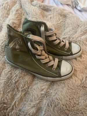Gröna high top sneakers från Replay - Snygga gröna high top sneakers från Replay med vita gummisulor och tåhättor. Skorna har vita snören, dragkedja på sidan och ett coolt mönster på insidan. Utsidan pryds av Replay-logga i nitar.