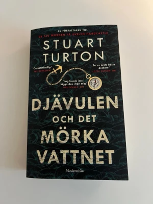 Djävulen och det mörka vattnet - Spännande deckare av Stuart Turton med svart och mörkgrönt omslag och stora beige bokstäver. Boken är i pocketformat och utgiven av Modernista. Handlingen utspelar sig på 1600-talet och bjuder på mysterier till havs.
