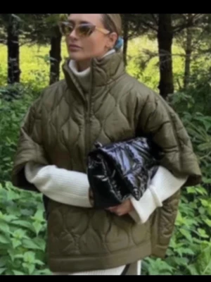 Grön poncho jacka - Stilren olivgrön dunväst med hög krage och korta ärmar. Västen har ett quiltat mönster och en boxig, oversized passform. Perfekt att bära över en stickad tröja för en trendig lager-på-lager-look.