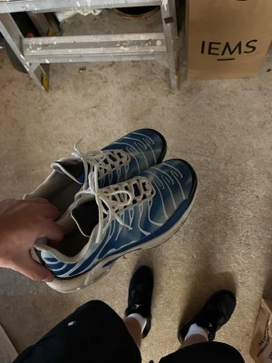  blå och vita sneakers - Säljer ett par sneakers i blått och vitt med vita snören och den klassiska vågdesignen på ovandelen. Skorna har en synlig Air-sula och svarta detaljer på sulan. Perfekta för dig som gillar sportig och retro stil.