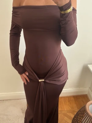 Brun offshoulder långklänning - En brun lång super fin långklänning perfekt till festliga tillfällen. Den är mjuk i materialet och använd endast en gång, där bak har den en scrunch vid rumpan som formar den fint.