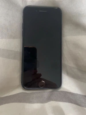 Svart iPhone 7 med rund hemknapp - Säljer en svart iPhone 7 med klassisk rund hemknapp och slimmad design. Baksidan är i matt aluminium med Apple-loggan och enkel kamera i hörnet. . Några repor på bak och framsidan funkar hur bra som helst.