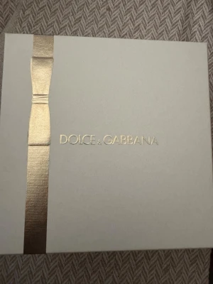 Dolce & Gabbana The One parfymset - Lyxigt parfymset från Dolce & Gabbana med doften The One. Setet innehåller en rektangulär glasflaska med guldfärgat lock och en matchande smal resestorlek, båda med elegant design. Kommer i en stilren ljus ask med gulddetaljer.