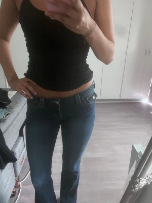 Blå bootcut jeans från True Religion - Säljer ett par blå bootcut jeans från True Religion med klassiska kontrastsömmar och snygga fickdetaljer bak. Jeansen har låg midja och är tillverkade i stretchigt denim för en bekväm passform. Perfekta för en trendig och avslappnad look. Har en liten defekt längst ner på jensen men inget man tänker på💕