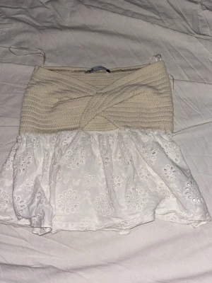 Vit och beige topp från Zara - Supersöt topp från Zara med beige ribbad överdel och vit volangig nederdel i broderad bomull. Omlott-detalj upptill och tunna axelband. Perfekt för en fräsch och somrig look!