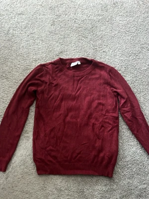 Vinröd stickad tröja från Vila - En enkel och snygg vinröd stickad tröja från Vila. Tröjan har rund halsringning, långa ärmar och ribbade muddar vid ärmslut och nederkant. Perfekt att matcha med jeans eller kjol. Aldrig använd. 