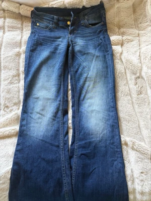 Blå bootcut jeans från Cheap Monday - Säljer ett par blå bootcut jeans från Cheap Monday med ikonisk orange patch bak. Jeansen har klassisk femficksmodell, låg midja och lätt slitningar framtill för en cool vintagekänsla. Tillverkade i denim med snygg tvätt och utställda ben.