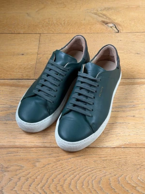 Axel Arigato Clean 90 - Grön - Strl 41 - Säljer ett par riktigt snygga Clean 90 från Axel Arigato i en mörkgrön färg. Tidlös modell i skinn med vit sula – en av Arigatos mest ikoniska sneakers. Skick: Mycket gott begagnat skick. Naturlig crease på tåboxen som förväntat vid användning, i övrigt inga anmärkningar. Sulan är knappt använd. 	•	Märke: Axel Arigato 	•	Modell: Clean 90 	•	Storlek: EU 41 	•	Färg: Mörkgrön 	•	Material: Läder 	•	Kartong: Medföljer ej Nypris: ca 2 400 kr Säljes utan returrätt. 