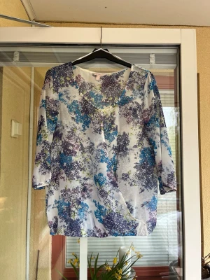 Blommig topp från Esprit  - Topp med blommigt mönster i blå, lila och gröna nyanser. Trekvartsärmar. Resår i nederkanten.