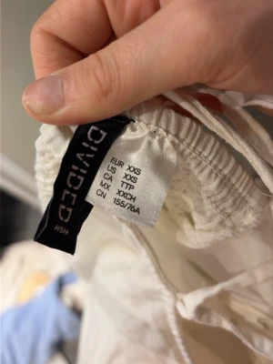 Vit kort klänning från H&M Divided - Supersöt vit kort klänning från H&M Divided med puffärmar, smockad rygg och knytband i ryggen. Klänningen har en romantisk vibe och är gjord i ett lätt material som känns luftigt och fräscht. Perfekt för varma dagar och somriga tillfällen.