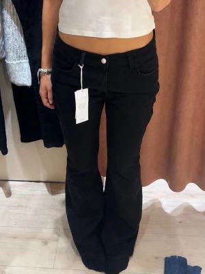 Svarta bootcut jeans låg midja - Snygga svarta bootcut jeans med låg midja och klassisk femficksdesign. Jeansen har en knapp och dragkedja framtill samt utsvängda ben. Perfekta för en trendig och avslappnad stil.