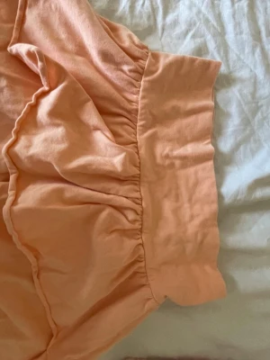 Ljus orange volangkjol i bomull - Söt kort kjol i ljus orange färg med bred midja och volangkant. Kjolen har en avslappnad passform och är tillverkad i mjuk bomull, perfekt för varma dagar. Enkel att matcha med både toppar och t-shirts.