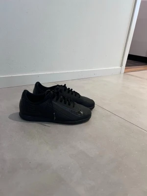 Svarta Nike sneakers med mönster - Säljer ett par helsvarta Nike skor med diskret mönster på ovandelen och klassisk låg siluett. Skorna har svarta skosnören och en svart sula. Perfekta för dig som gillar stilrena och sportiga skor.2 år gammla